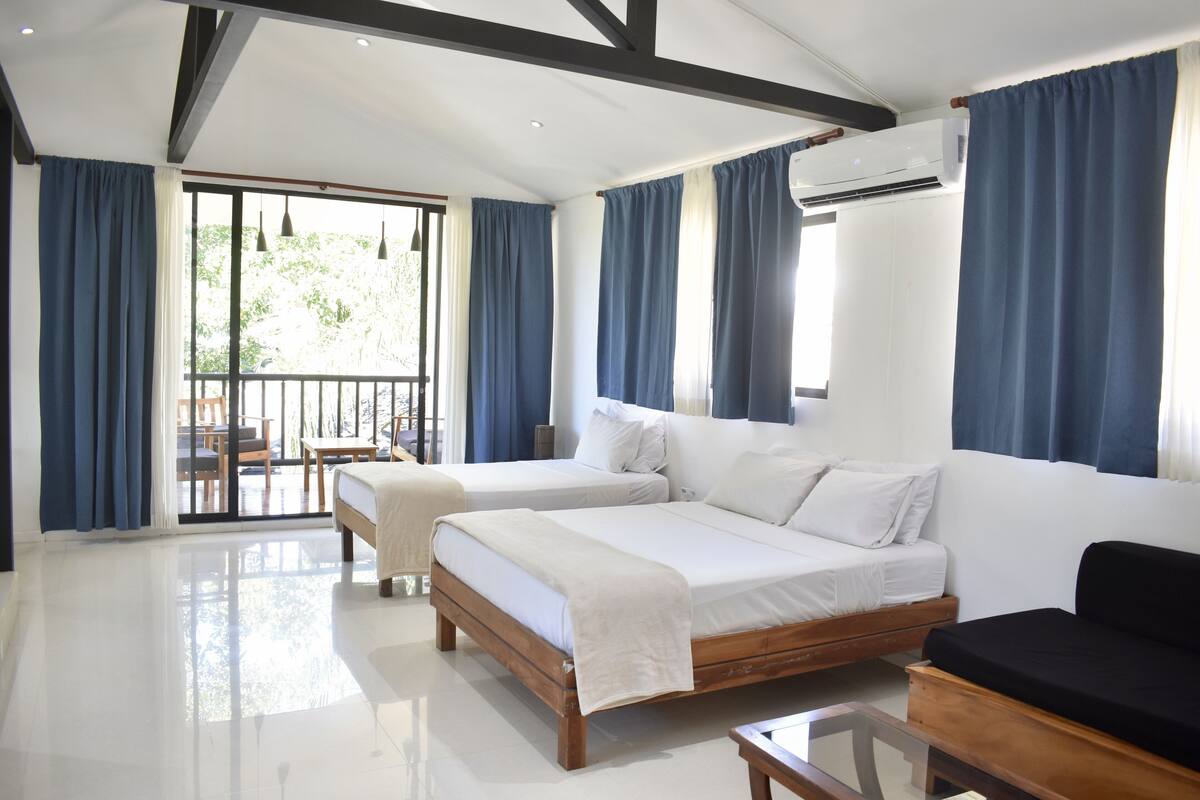 Una habitación de hotel moderna con dos camas, un sofá y un balcón con una mesa y sillas.