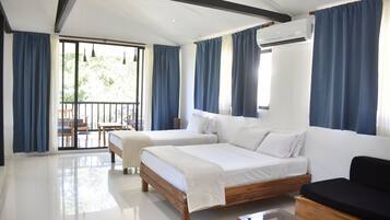 A modern hotel room with two beds, a sofa, and a balcony with a table and chairs.
