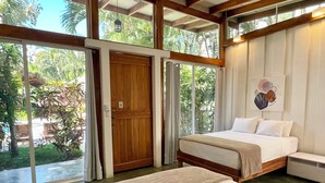Een slaapkamer met een groot bed, een houten deur en uitzicht op groen.