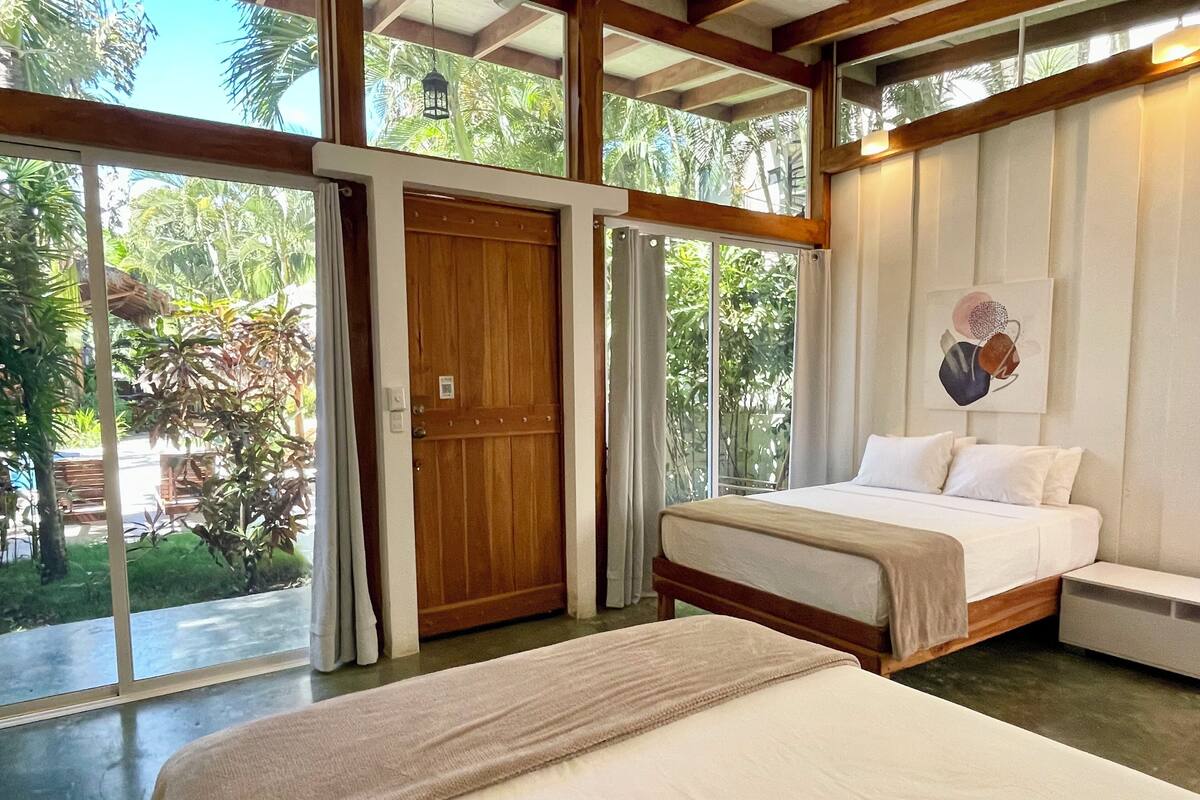 Un dormitorio con una cama grande, una puerta de madera y vistas a la vegetación exterior.