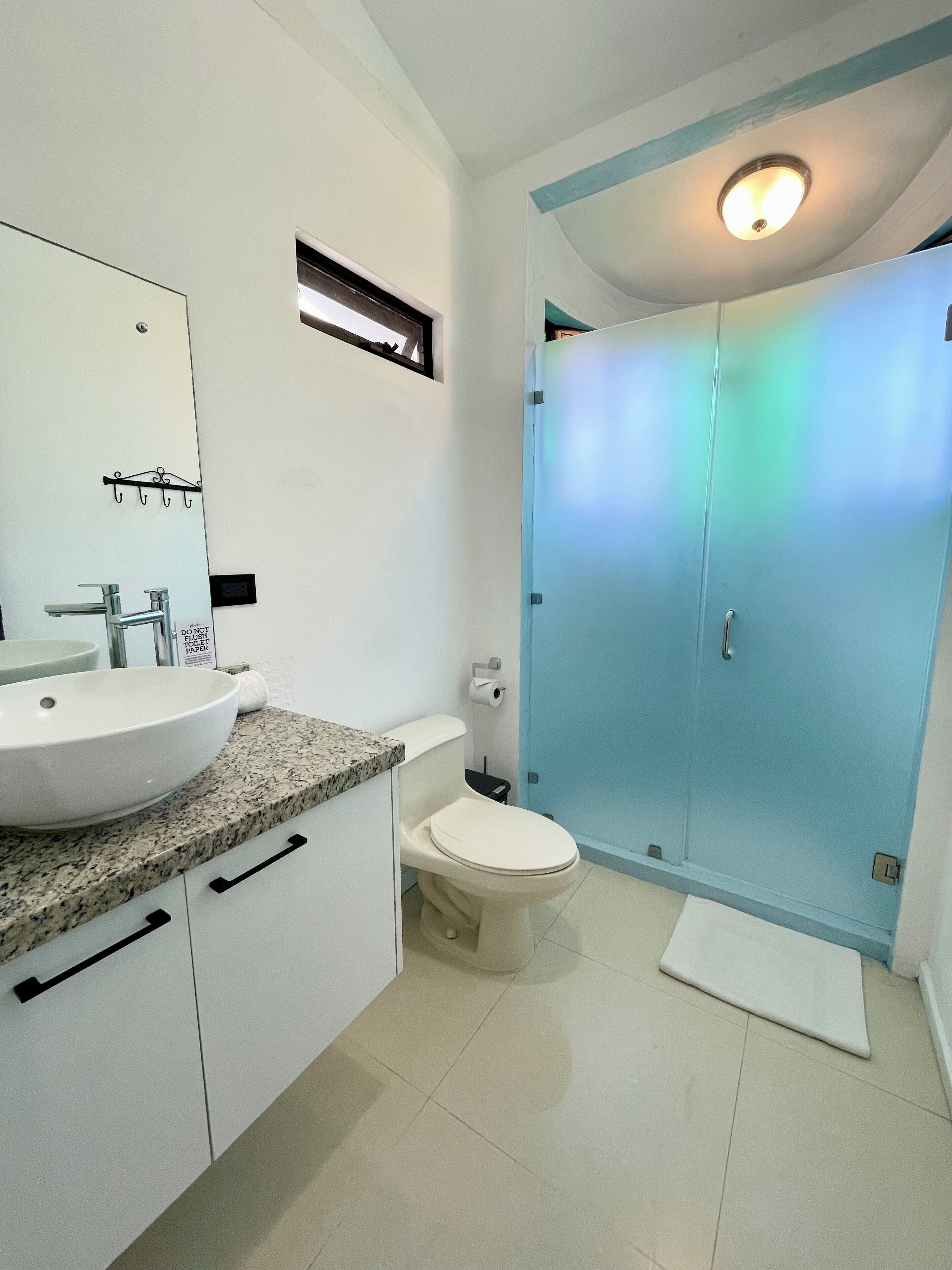 A bathroom with a white sink, mirror, and toilet. There is a shower with frosted glass doors.
