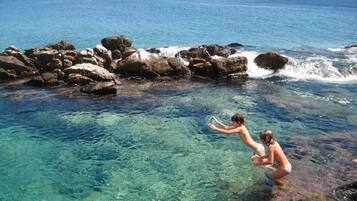 A clear coastal water body with rocky formations and a distant view of the ocean.