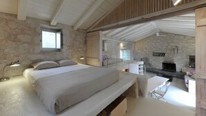 Une chambre avec un mur en pierre, un plafond en bois, un lit, un bureau et une cheminée.