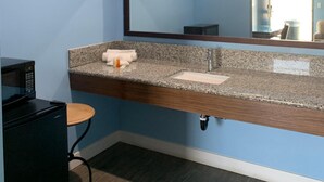 A bathroom with a granite countertop, a sink, a mirror, a towel, and a microwave. - Redondo Beach Motel (Gardena)
