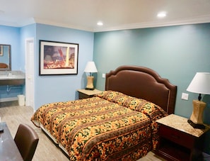 A hotel room with a bed, two bedside tables with lamps, a framed picture on the wall, and a bathroom visible through an open door. - Redondo Beach Motel (Gardena)