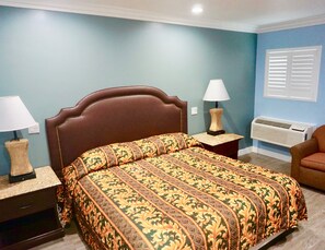 A bedroom with a bed, two bedside lamps, an air conditioner, and a chair. - Redondo Beach Motel (Gardena)
