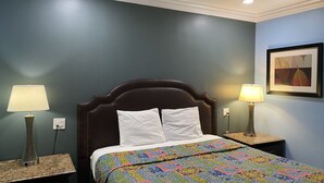 A neatly made bed with a colorful quilt, two bedside lamps, and a framed artwork on the wall. - Redondo Beach Motel (Gardena)