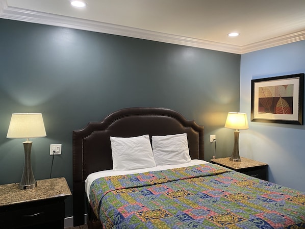 A neatly made bed with a colorful quilt, two bedside lamps, and a framed artwork on the wall. - Redondo Beach Motel (Gardena)