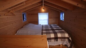 A wooden cabin room with a bed, a small table, and two windows. - A small cottage in the center of Horta, Faial Island, Azores (Horta)