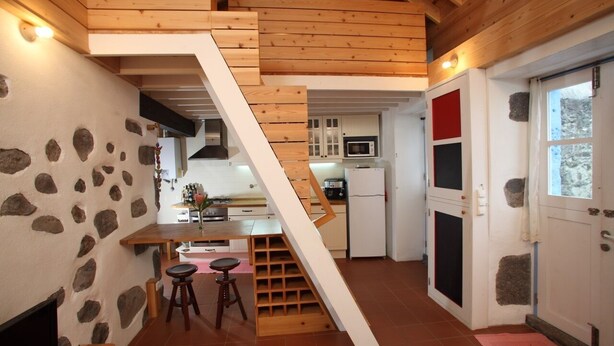 A kitchen with a wooden staircase, stone walls, and a view of the dining area. - A small cottage in the center of Horta, Faial Island, Azores (Horta)