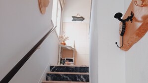 A staircase with black and white marble steps leading to a room with a white wall, a welcome sign, and a wooden coat rack. - Tia Rosário Casita in Lourinhã (Lourinhã)