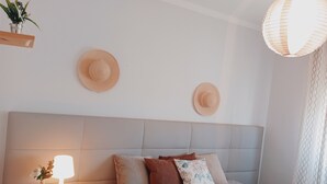 A bedroom with a bed, a bedside table with a lamp, two hats on the wall, and a hanging light fixture. - Tia Rosário Casita in Lourinhã (Lourinhã)