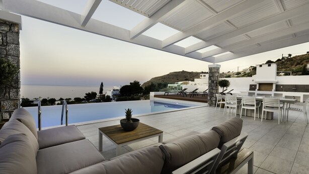 Un espacio lounge moderno al aire libre con piscina, asientos y vista al mar.
