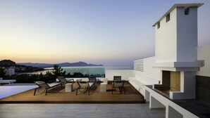 Una terraza en la azotea con mobiliario exterior, una piscina y vistas al mar y montañas a lo lejos.