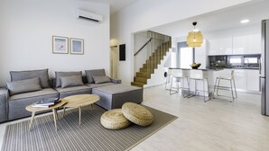 Una sala moderna con un sofá gris, una mesa de centro de madera y una escalera que lleva a una zona de cocina.