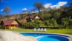 A resort with a swimming pool, two wooden cabins, and a grassy area with lounge chairs. - Ecolodge Don Felix (Santa Ana)