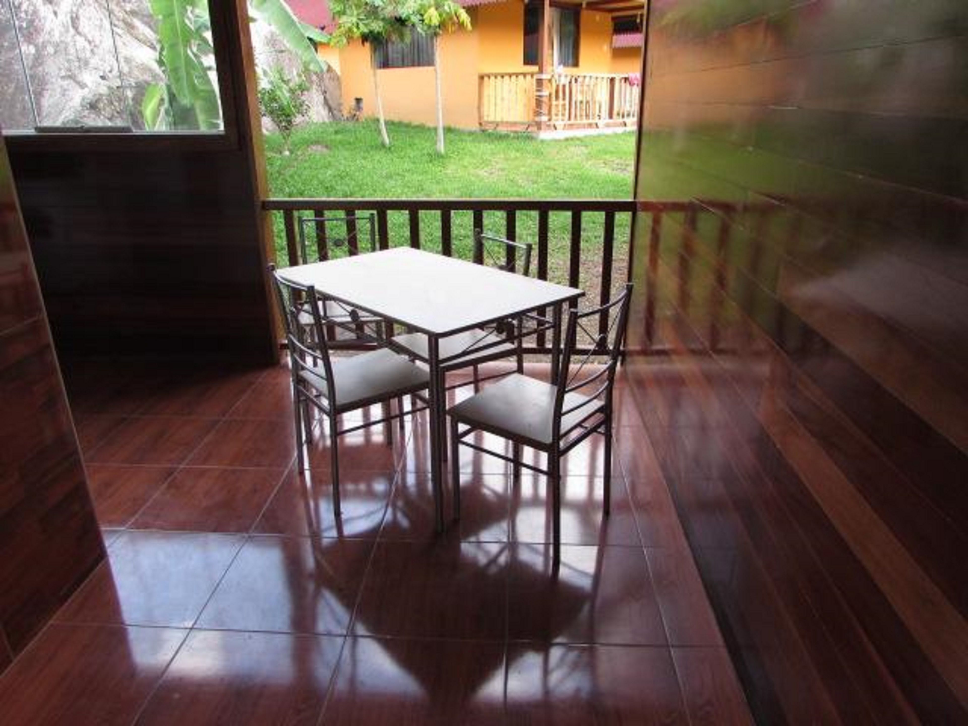 Una habitación con suelo de baldosas, una mesa blanca con cuatro sillas y vistas a un edificio amarillo con balcón.