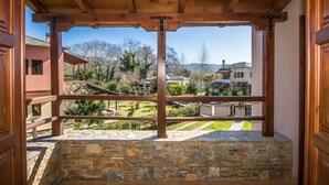 A covered outdoor area with stone walls and wooden beams, overlooking a landscaped garden and neighboring houses.