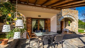 An outdoor patio with stone flooring, wicker furniture, and a hanging metal planter with flowers.