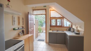 A compact kitchen with a stove, sink, and cabinets. There is a window with a view of greenery outside. - Avra Apartments, Maistros (Καλύβες)