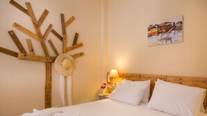 A hotel room with a bed, a wooden wall art piece, a straw hat, and a painting on the wall. - Avra Apartments, Maistros (Καλύβες)