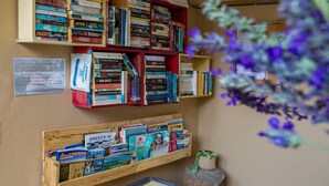A bookshelf filled with books, a wooden shelf with magazines, and a small plant on a tree stump. - Avra Apartments, Maistros (Καλύβες)