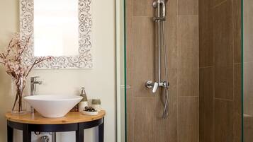 A bathroom with a wooden vanity, a white sink, a mirror with an ornate frame, and a glass-enclosed shower area.