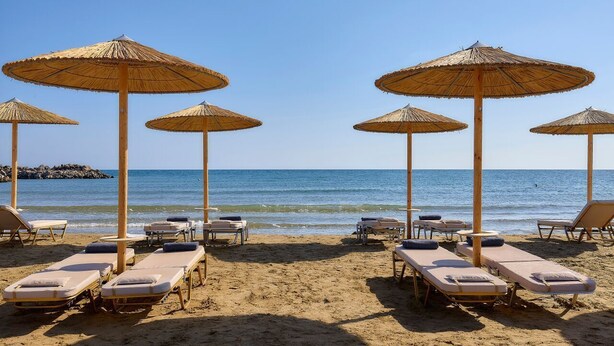 A beach with sun loungers and thatched umbrellas.