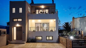 A modern two-story house with a balcony, a door, and a small garden area.