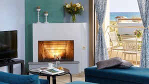 A living room with a fireplace, a TV, and a view of the sea.