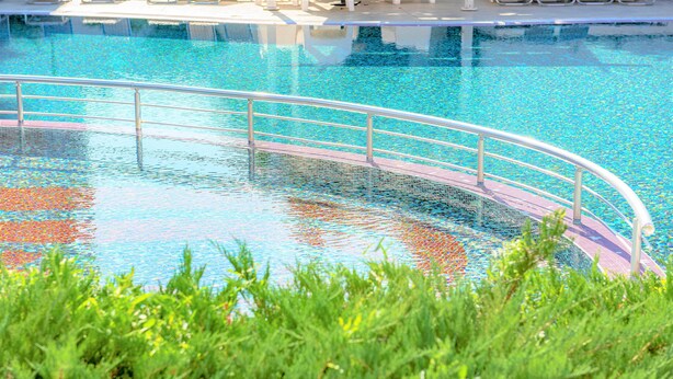 A swimming pool with a metal railing and a clear blue water surface.