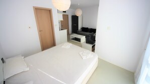 A modern bedroom with a large bed, a wooden door, a small kitchenette, and a seating area with a sofa.