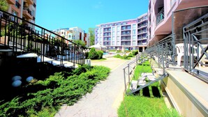 A pathway leading to a residential building with balconies, a swimming pool, and a well-maintained garden.