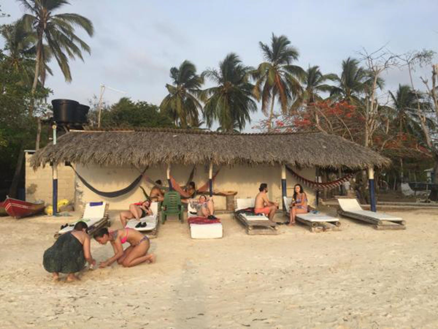 Eine Strandhütte mit Reetdach, einer Hängematte und mehreren Liegestühlen.
