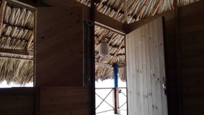 A wooden room with a thatched roof, a visible door, and a view of an outdoor area. - Dahlandia (Isla Mucura)