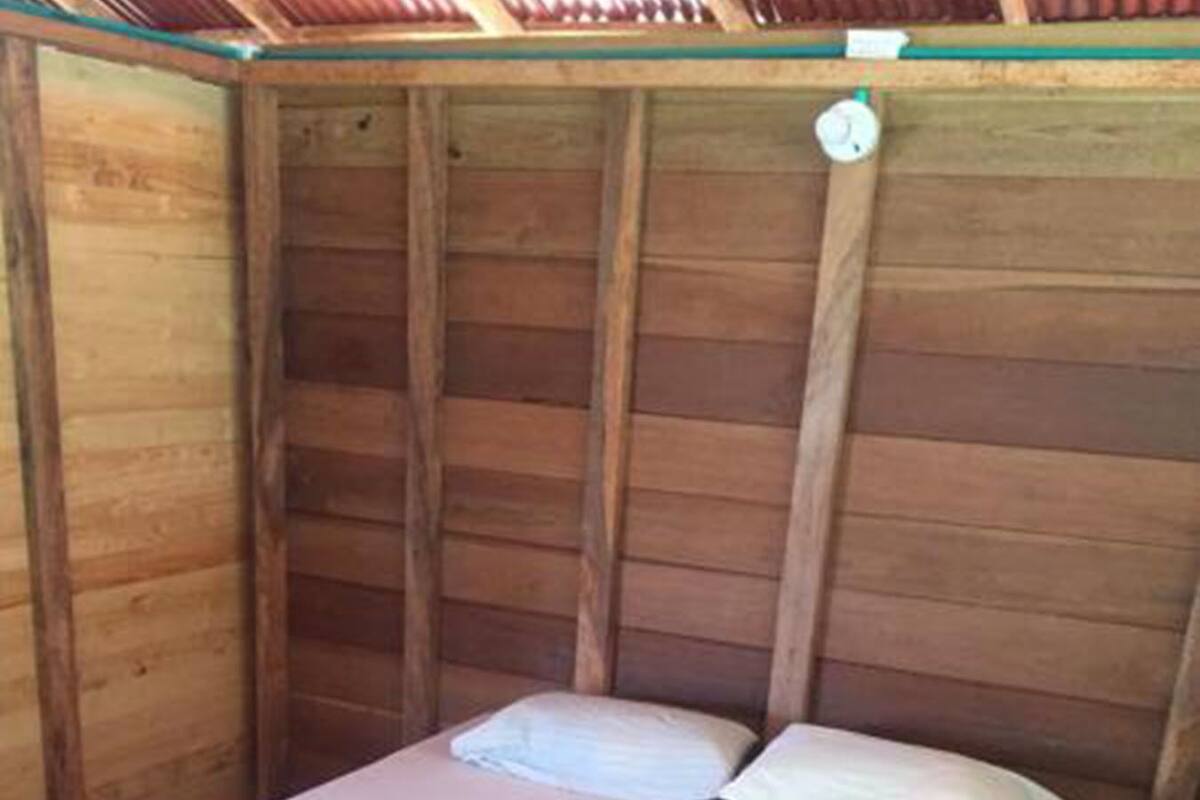 Ein Einzelbett mit weißer Matratze und Kissen, ein zusammengerolltes Handtuch und eine kleine Uhr an der Wand.
