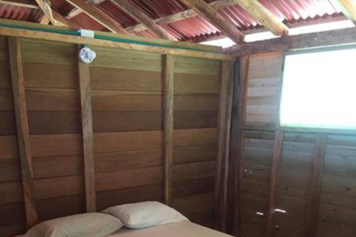 Ein Einzelbett mit Matratze und Kissen in einem Zimmer mit Holzwänden und schrägem Dach.