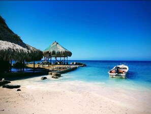 Uma praia com uma cabana de palha e um barco atracado perto da margem.
