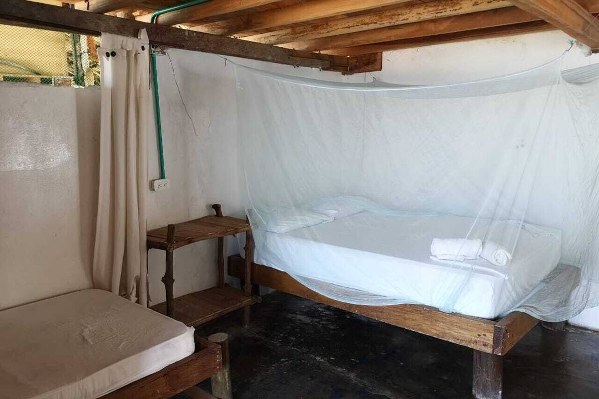 Ein schlichtes Zimmer mit einem Moskitonetz über dem Bett, einer hölzernen Bank und einem Vorhang.
