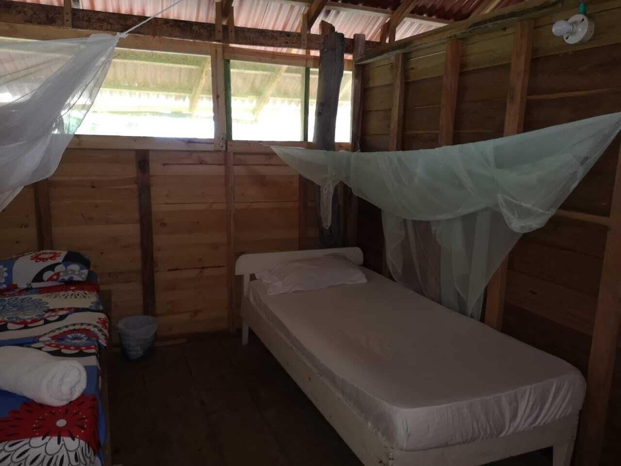 A small, wooden room with a single bed, a small table, and a mosquito net over the bed.