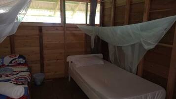 A small, wooden room with a single bed, a small table, and a mosquito net over the bed.