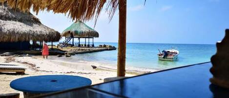 A beach with thatched-roof huts, a boat, and a clear blue sky.
