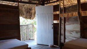 A room with two beds, a wooden door, and a thatched roof. - Dahlandia (Isla Mucura)