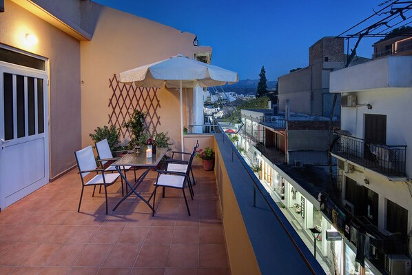 A balcony with a table and chairs, a white umbrella, and potted plants.
