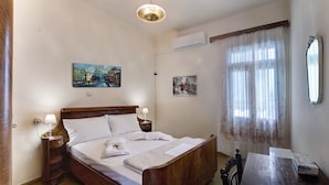 Habitació d'hotel amb un llit de fusta, dues taules de nit amb làmpades, una finestra gran amb cortines de tul, i dos quadres penjats a la paret.
