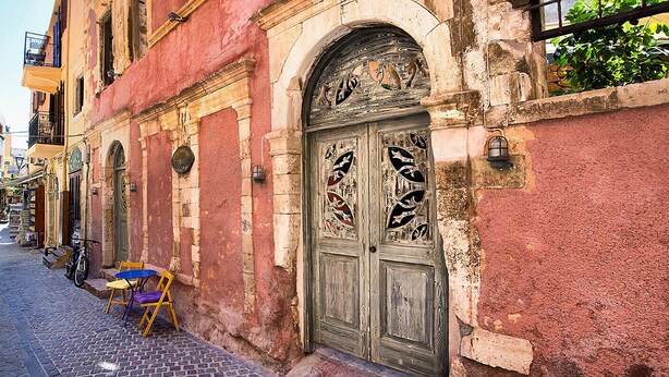 Un edifici històric amb una gran porta de fusta ornamentada, una bicicleta aparcada a l'exterior i una taula petita amb cadires a la vorera.