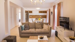 Ein modernes Wohnzimmer mit einer Couch, einem Couchtisch, einem Fernseher und einer Küche im Hintergrund.