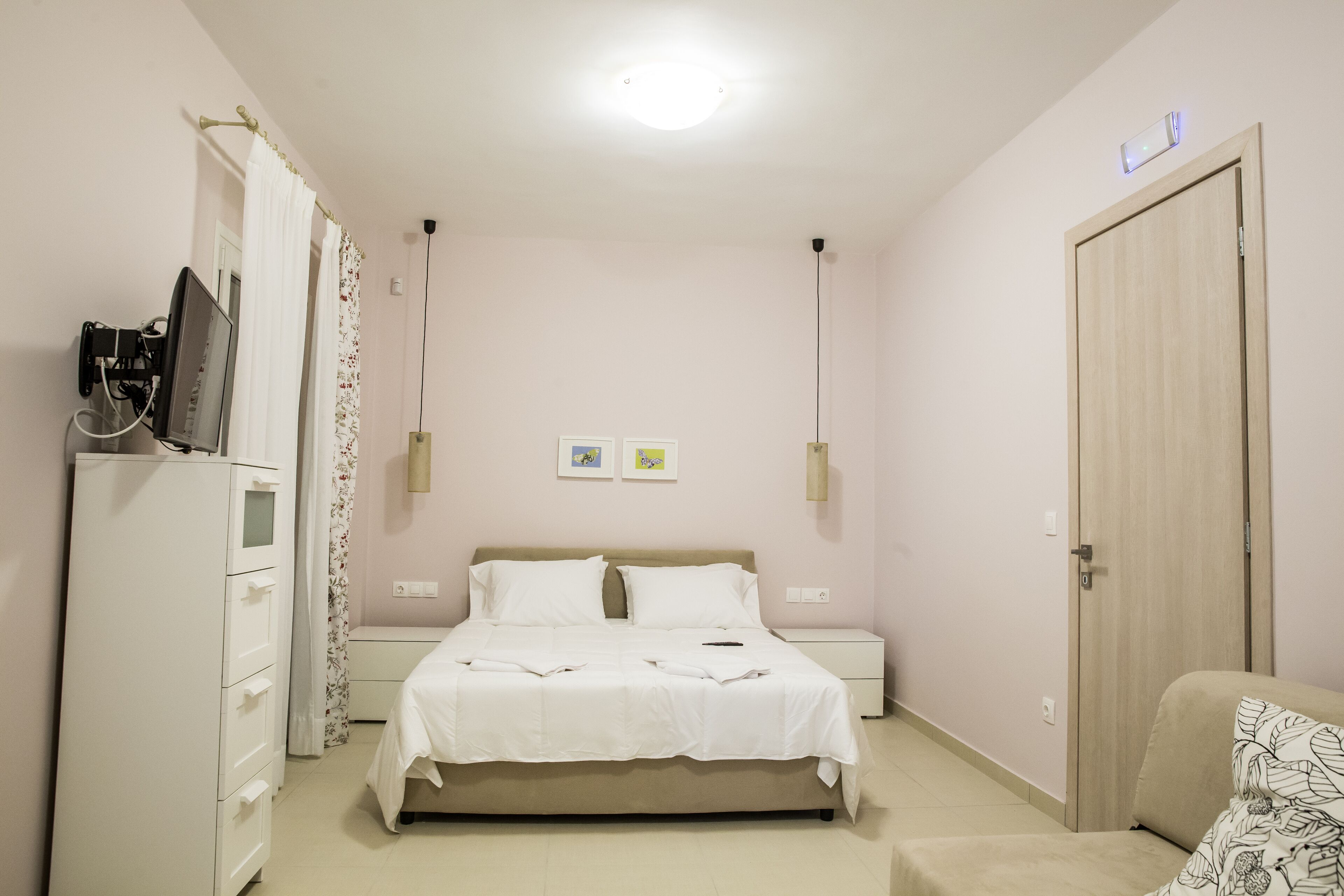 A bedroom with a bed, bedside tables, a wardrobe, a television, and a door.