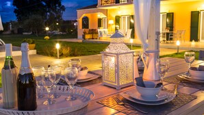 Ein Essbereich im Freien mit Tisch, gedeckt für eine Mahlzeit, inklusive Weingläsern, Tellern und einer Karaffe.