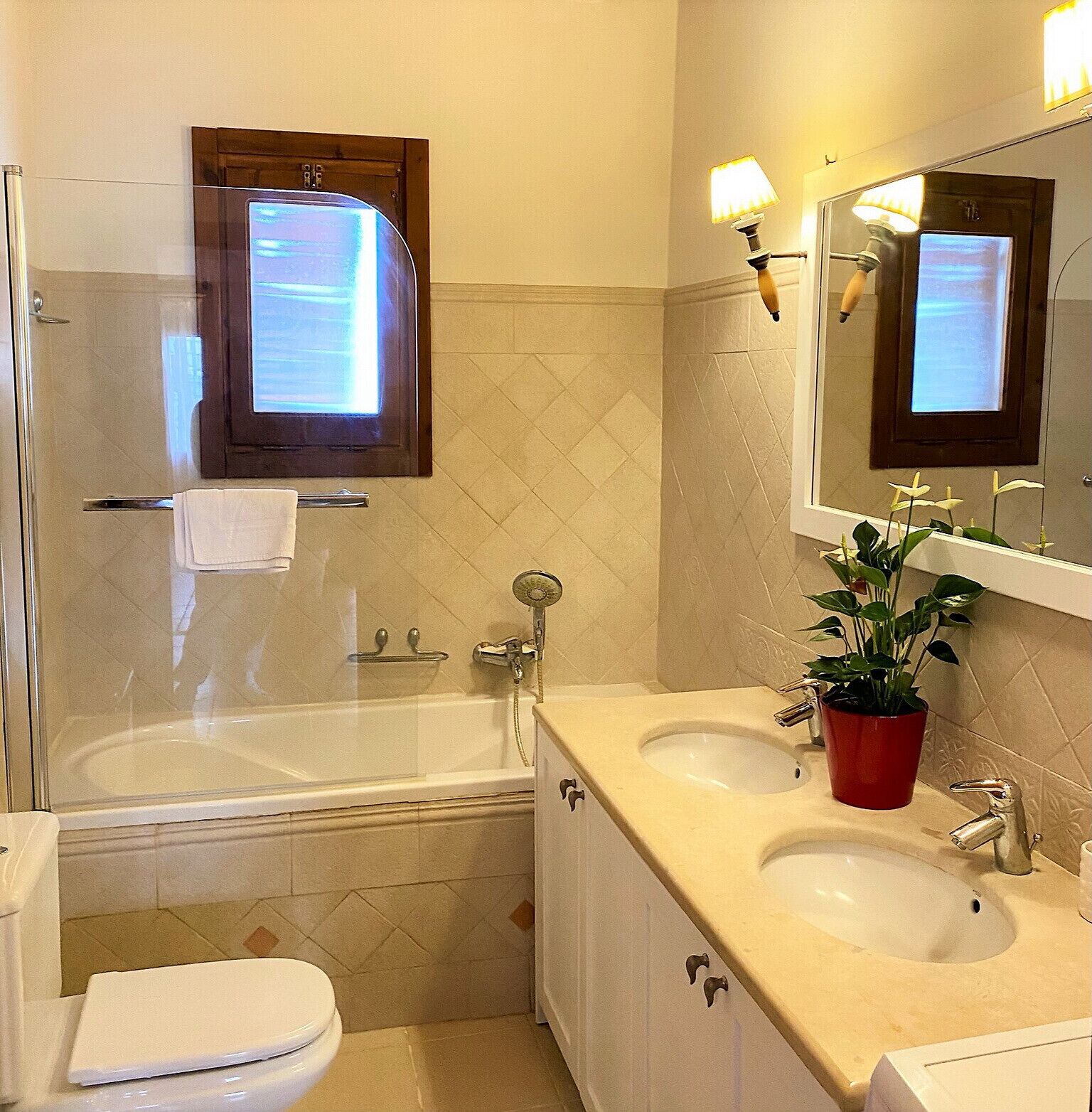 A bathroom with a bathtub, two sinks, a toilet, a shower, and a mirror with lights.